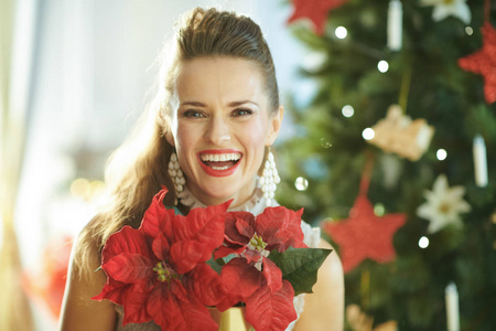 圣诞树旁有红色一品红的微笑时髦女人肖像
