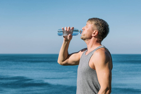 一个人在一次锻炼后，从大海上的瓶子里喝着水，往脸上倒水，令人耳目一新