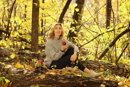 在秋季公园与落叶的背景针织毛衣的年轻美丽的女孩