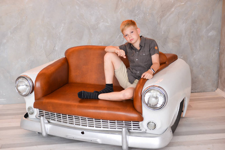 男孩坐在工作室的内部的椅子上的复古汽车的形式。创意复古家具