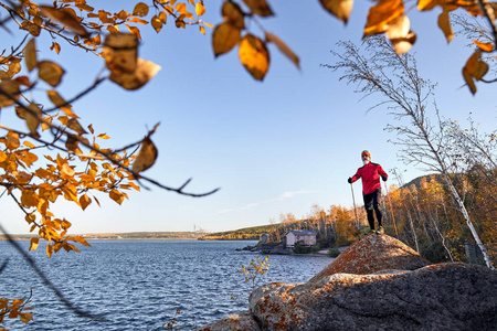 秋天的时候，长胡子的人穿着红色衬衫，两根徒步旅行的杆子站在湖边。 跟踪运行概念