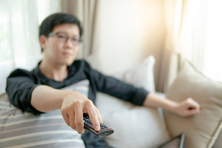 在家庭影院房间的沙发上看电视时，用遥控器关闭男性亚洲手。 家庭生活和放松的生活方式概念。