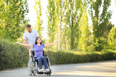 轮椅上快乐的年轻女子和她的丈夫在户外