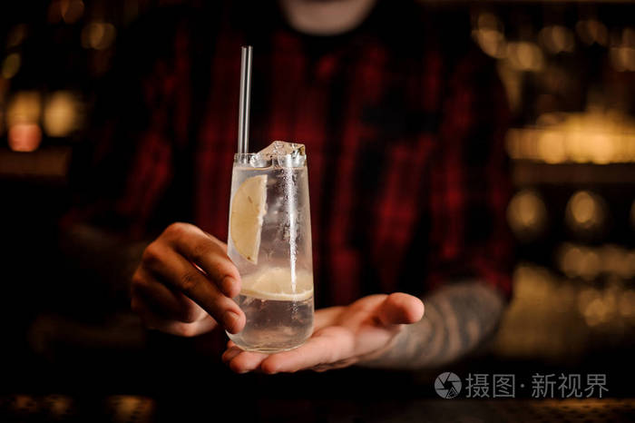 照片 酒保拿着装满汤姆柯林斯鸡尾酒的长杯酒杯,在灯光模糊的背景下.