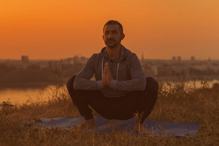 男人在日落时做瑜伽，用城市视野佛教佛塔姿势。色调的图像。