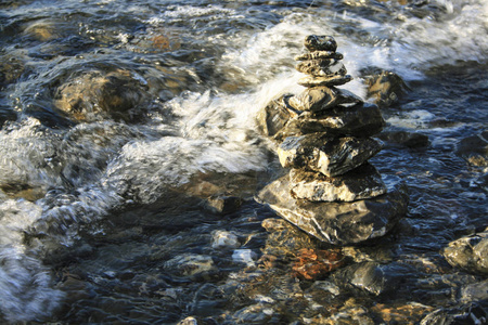 海浪前的石塔。 几块石头站在水旁边。 泡沫波接近石塔。 太阳又反射在滚滚的水中。
