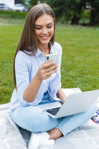在公园户外使用笔记本电脑和手机的漂亮年轻漂亮女人的形象。