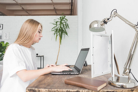年轻的女商人在家里的笔记本电脑后面工作。创意斯堪的纳维亚风格的工作空间