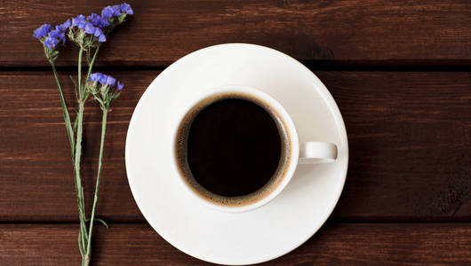 黑木桌背景上放着鲜花的咖啡杯