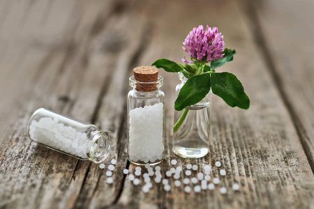 顺势颗粒在小玻璃瓶中，一些颗粒散落在旧木桌和一朵小花上。