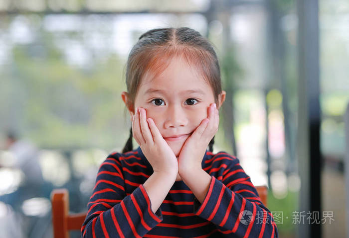 微笑的亚洲小女孩,抚摸着她的脸颊,直视着坐在咖啡馆里的相机.