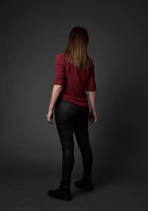 穿红色衬衫和皮裤的深色女孩的全长肖像。站立姿势，灰色工作室背景。