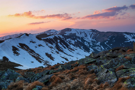 从草坪上可以看到覆盖着雪的镐头，被早晨的阳光照亮的山脉全景。日出。迷人的春天景观..