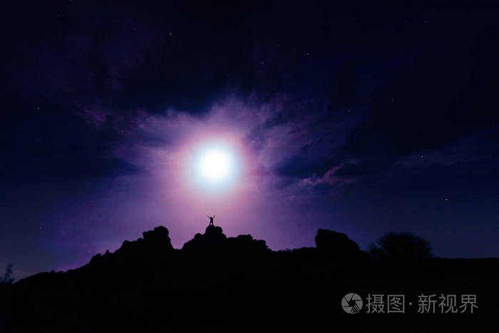在多云的月光下的夜空下的人. 一个男性身影站在岩石