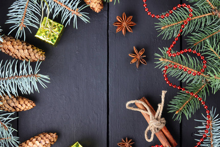 带有杉树枝和松果的圣诞节图案。肉桂棒，八角和杉枝在黑暗的木板上。圣诞树枝冷杉锥和木板上的红色项链