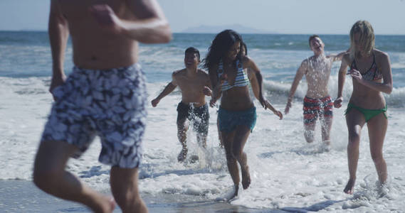 一群跨种族的年轻人，从海滩的水中奔跑