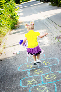 手拿玩具的金发小女孩在街上玩跳楼游戏