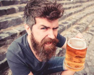 喝着冰镇啤酒休息的家伙。时髦的人在欢快的脸上喝着啤酒户外, 举杯干杯。欢呼的概念。坐在石头台阶上的胡子和胡子的人拿着啤酒玻璃
