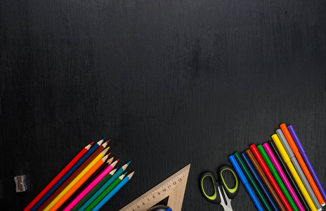 从上面看到彩色铅笔和黑色表面的各种学校用品