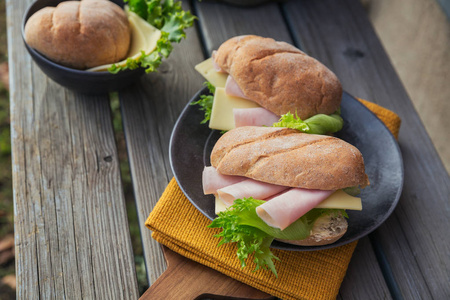 两个新鲜的西巴塔袋式三明治与火腿奶酪和生菜在乡村木制背景。 户外野餐的生活方式。
