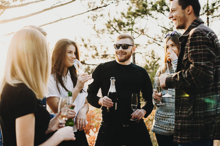 一群年轻的男人和女人在阳光明媚的白天站在美丽的大自然中，享受着香槟和彼此交谈