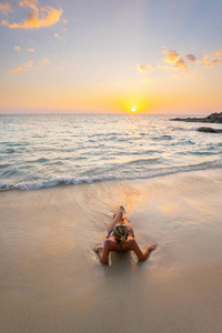 日落时穿着泳装在沙滩上的美丽年轻女子