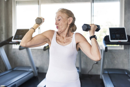 老年妇女在健身健身房锻炼提升哑铃。