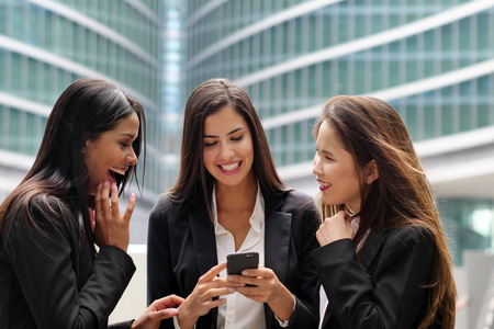 三位不同种族的商界女性亚洲欧洲和非裔美国人看着电话，微笑着。 概念社交网络团队业务人员和女性职业。