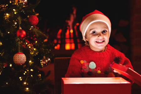 在圣诞节，一个小女孩在圣诞树下打开她的礼物，当她打开礼物时，她像魔法一样亮起。 概念魔术圣诞礼物假日幸福爱情。