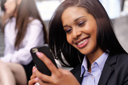 一个美国黑人商业妇女，她很高兴和微笑，同时发送信息，工作电子邮件或打电话使用办公室外的电话。 概念技术网络成功。
