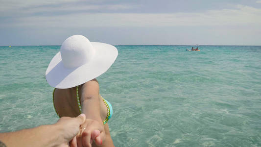 一个美丽的年轻女孩女人在海上的肖像，穿着泳衣，戴着一顶白色的帽子，牵着心爱的男人的手，大海背景。 概念海上清洁空气自由旅行