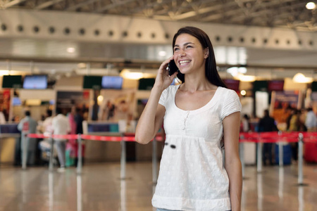 机场一个年轻的旅游女孩的肖像，等待她的航班，在电话里写着一条信息，微笑着，飞机。概念去周游世界，度假，度假..