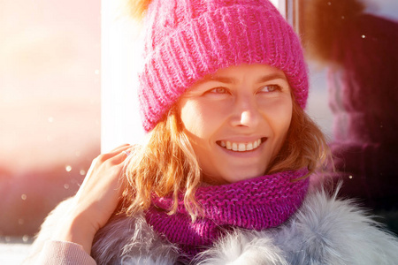 冬季背景上的肖像美女模特。美丽的现代年轻女子，戴着粉红色的针织帽，温暖的双手，微笑，远离视线，在寒冷的冬天散步。
