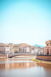 垂直照片，在Arno河上观看。 河流穿过著名的意大利托斯卡纳镇比萨。 建筑物在水的两边都是可见的。 山丘和岩石在清澈的天空中可以