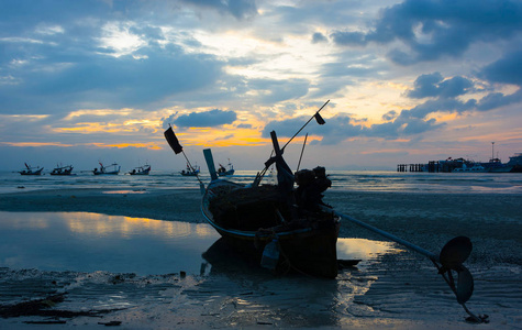 渔人长尾船停泊在晚潮滩上，傍晚时分两天，海滨和码头背景