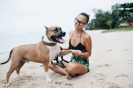 快活的，漂亮的年轻女人在海滩上坐着拥抱她的狗