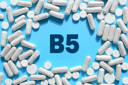 维生素B5文本在白色胶囊框架上的蓝色背景。 含有泛酸的药丸。 膳食补充剂和药物