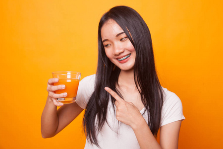 年轻的亚洲女人在明亮的黄色背景上指着橙汁