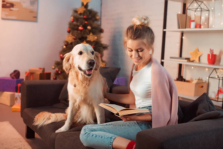 圣诞节的时候，美丽的金发女郎和金色的猎犬坐在沙发上看书