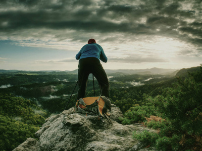 摄影师穿着蓝色运动衫，用镜子相机和三脚架在岩石的顶峰上工作。梦幻的雾状景观..