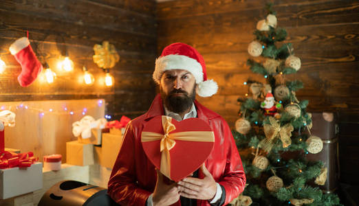 带着胡子的现代圣诞老人祝圣诞快乐, 新年快乐。圣诞老人穿着现代红色夹克。新年礼物盒里的礼物。圣诞节的家