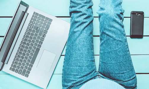现代女孩坐在蓝色的木制地板上，用笔记本电脑。 一代Z.自由职业者的概念。 工作空间。 上面的风景。