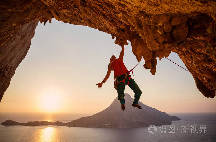 日落时,一只手挂在悬崖上的雄性攀岩者. 卡利姆诺斯岛