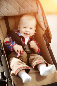 可爱的微笑的小婴儿坐在城市街道上的婴儿马车里。 微笑，微笑