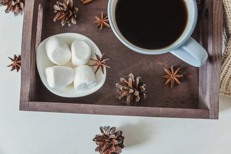 杯咖啡在乡村木制托盘甜棉花糖松果肉桂棒。 舒适的秋冬周末或假日在家。 带热饮料杯的家庭装饰。 潮晨风格概念