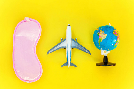平躺着飞机睡眠眼罩和地球仪在黄色五颜六色的现代时尚背景。 度假旅行暑假周末海上冒险旅行概念