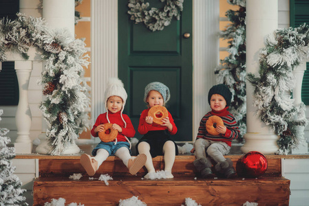 坐在他们家门廊上的孩子们的画像一起吃百吉饼。 圣诞快乐新年快乐。 院子里有圣诞树灯和装饰品。 奇迹时刻。