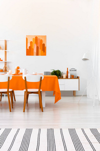 条纹地毯和海报在白色餐厅内部与木制椅子在橙色桌子。 真实照片
