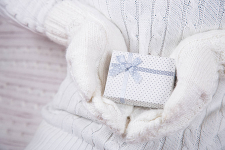 手拿白色针织手套，手拿可爱的礼品盒。 圣诞礼物。 新年贺卡。