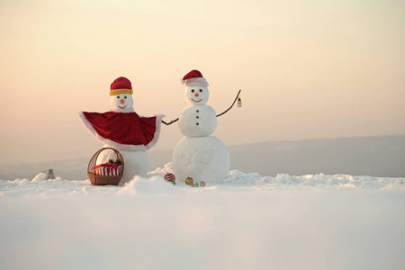 圣诞老人帽子在冬天。 圣诞节或圣诞节装饰玩具。 节日快乐和庆祝。 新年雪人从雪地上戴着圣诞帽。 雪人夫妇带着礼物盒在篮子里。 复